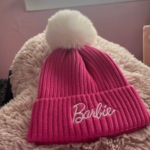 Barbie pink hat with white puff ball on top with barbie lettering on the front.